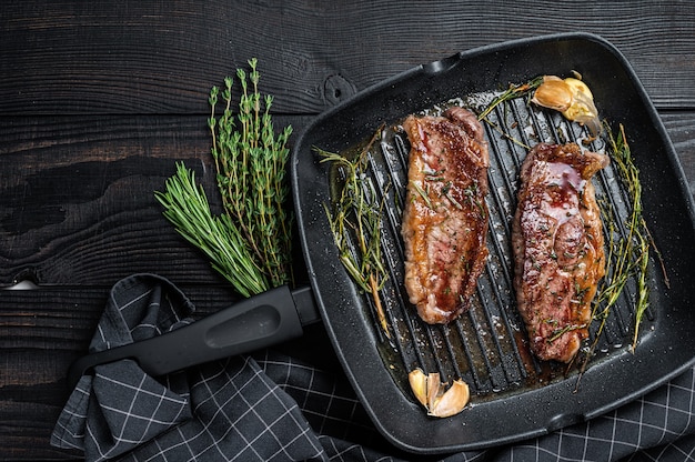 Grilled Prime Black Angus beef steaks Striploin or New York in a grill pan. Dark wooden background. Top view. Copy space.