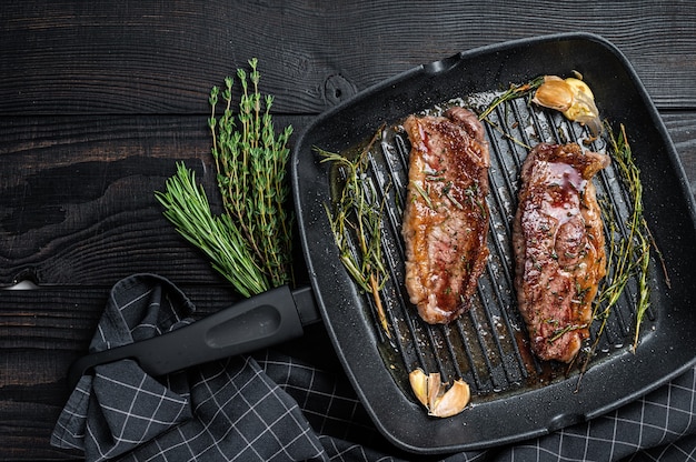 Bistecche di manzo black angus prime alla griglia controfiletto o new york in una padella per grigliare. fondo in legno scuro. vista dall'alto. copia spazio.