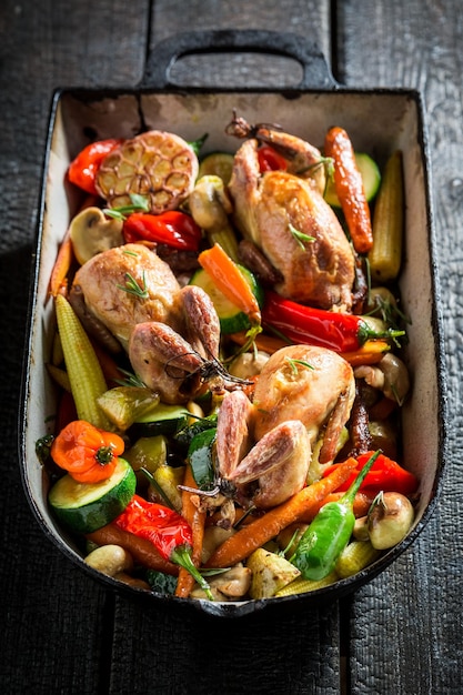 Grilled quails with vegetables in casserole on dark background