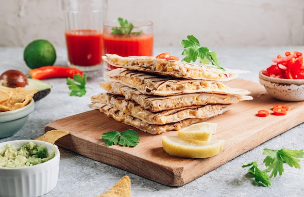 Grilled quesadillas on wooden board and with salsa and guacamole on stone background Mexican cuisine concept Quesadilla wrap with chicken and corn Selective focus