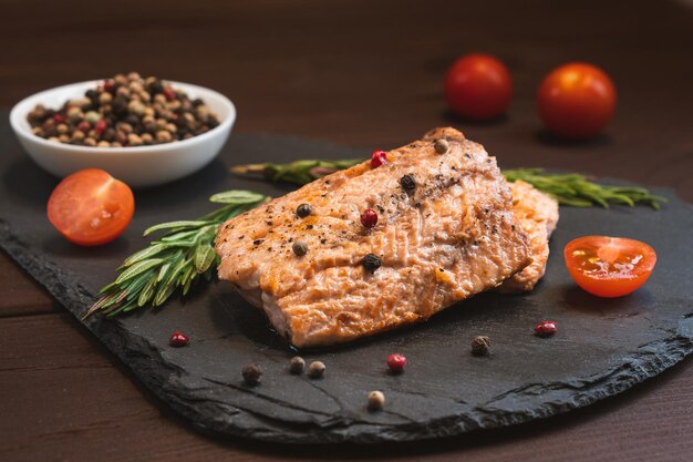 검은 돌 배경에 토마토 로즈마리와 향신료를 곁들인 구운 붉은 생선 연어 스테이크