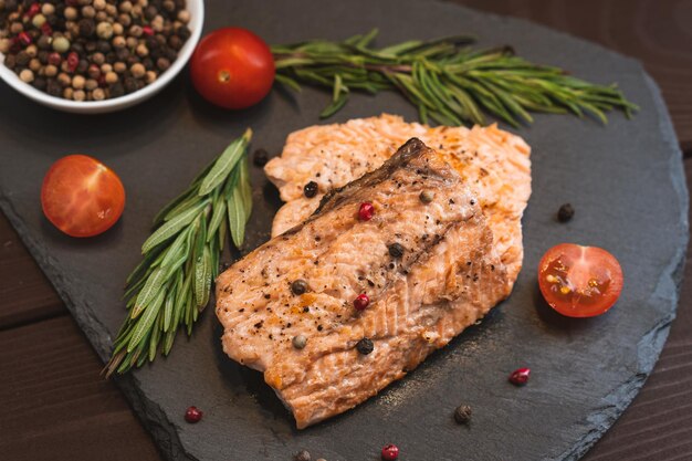 Grilled red fish meat salmon steak with tomato rosemary and spices on black stone background