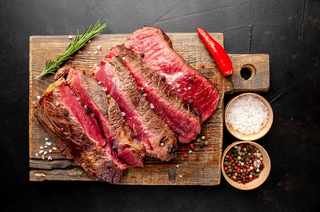 Grilled rib eye beef steak with herbs and spices on a stone background