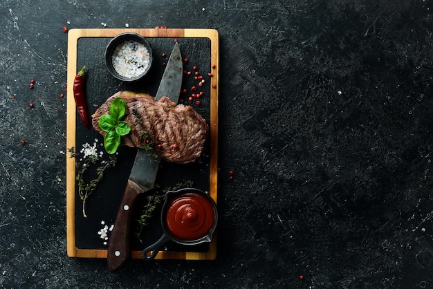 Grilled rib eye steak herbs and spices On a black stone background