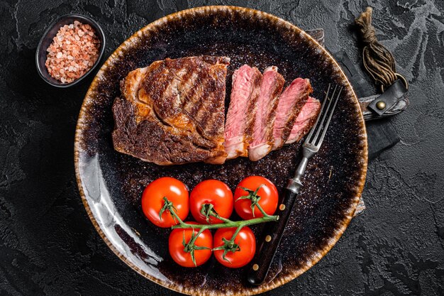 Bistecca alla griglia ribeye carne marmorizzata di manzo su un piatto con pomodoro vista dall'alto su sfondo nero