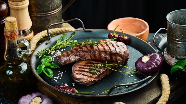 Bistecca di manzo alla griglia con erbe aromatiche e spezie su un tavolo scuro vista dall'alto spazio libero per il testo