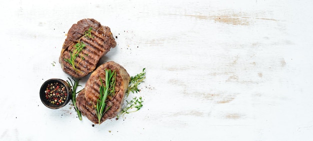 Photo grilled ribeye beef steak herbs and spices on a white wooden background top view free space for your text