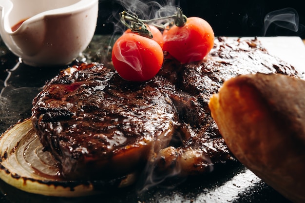 Grilled ribeye beef steak served on stone board with tomatoes bread and sauce