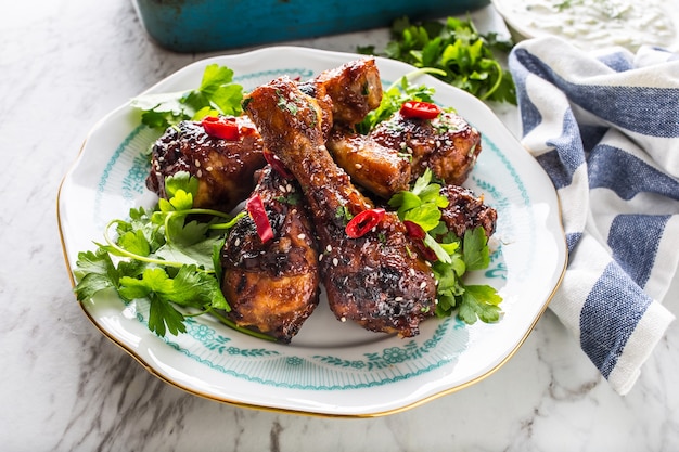 Grilled roasted and barbecue chicken legs on white plate with herb decoration.