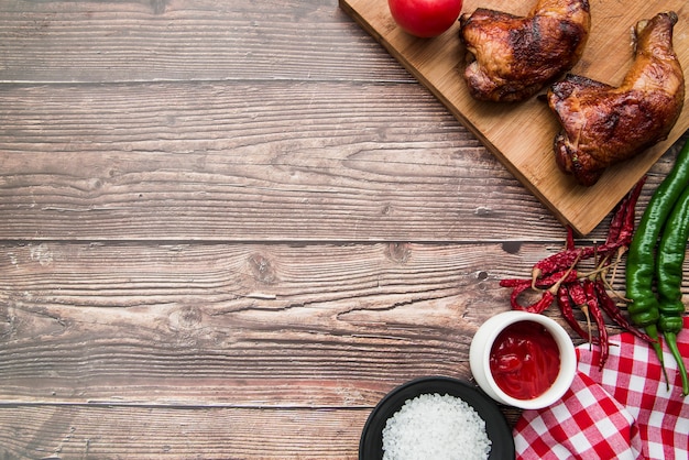 Photo grilled roasted chicken leg with chilies; salt; sauce and napkin on desk