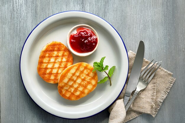 Grilled round slices of Greek cheese with cowberry jam, fresh mint and coriander leaves. Flat lay on light grey wood