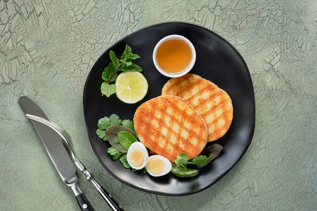 Grilled round slices of Greek cheese with honey, fresh mint and coriander leaves. Flat lay on green textured table