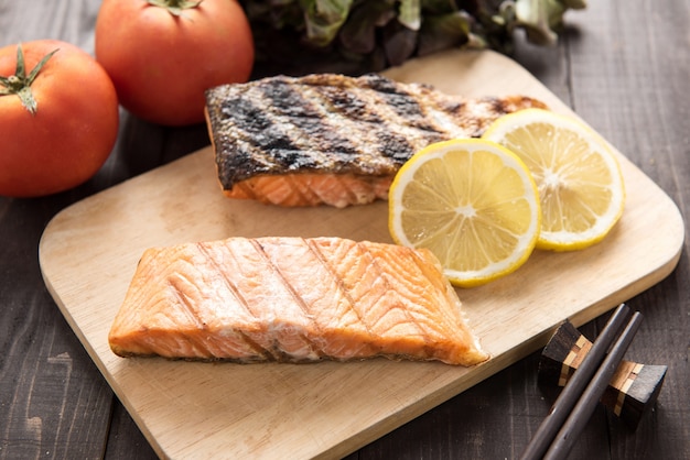 Grilled salmon on cutting board on wooden table.