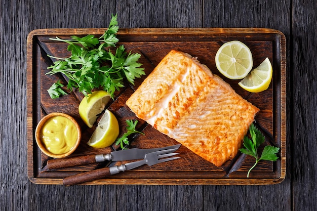 Grilled salmon fillet on a rude wooden cutting board with mustard and lemon