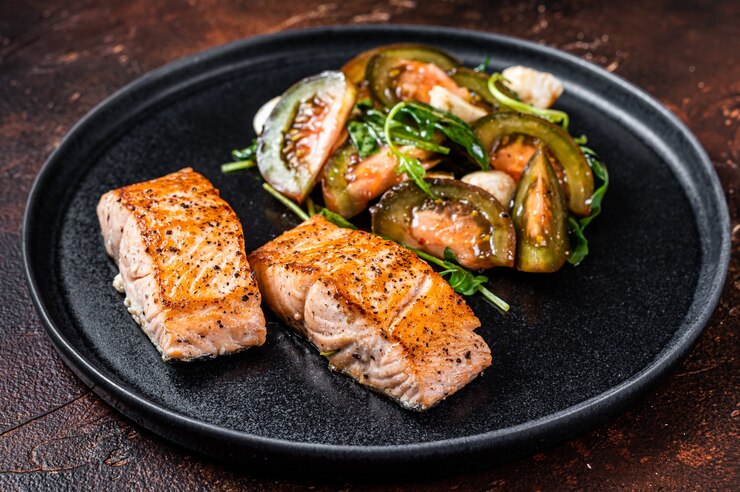 Photo grilled salmon fillet steaks with arugula and tomato salad on a plate. dark background. top view.