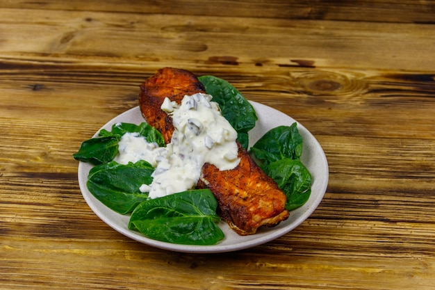 Grilled salmon fillet with spinach and tartare sauce on wooden table