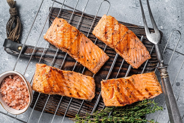 Grilled salmon fillets steaks with salt pepper and herb on grill. Gray background. Top view.