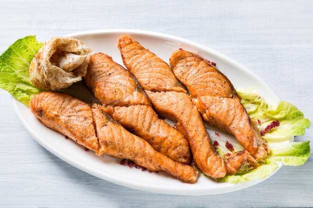 Жареные кусочки лосося на белой тарелке с салатом и блинчиком