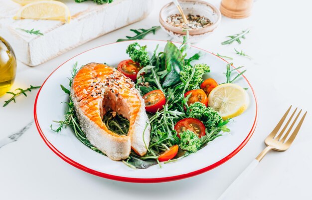 グリルしたサーモンステーキと新鮮な野菜のサラダ、白い大理石の背景にレモン。健康食品のコンセプト