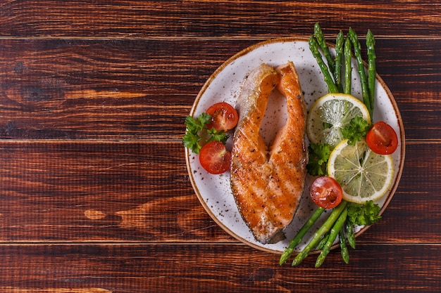 Grilled salmon steak served with asparagus, tomato and lemon.