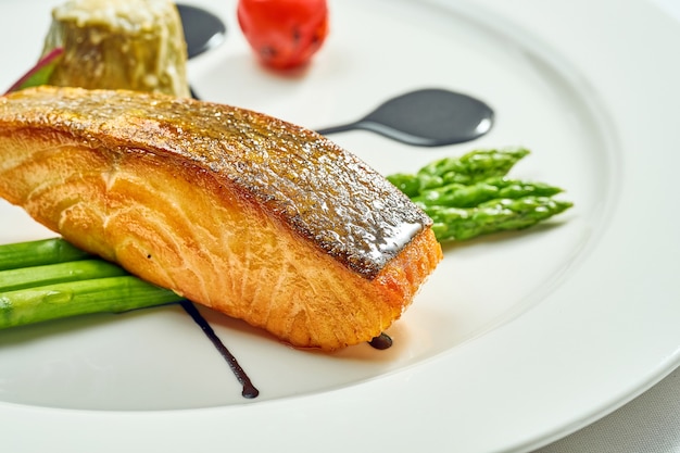 Grilled salmon steak with asparagus and balsamic sauce in a white plate. Isolated on white surface. View from above