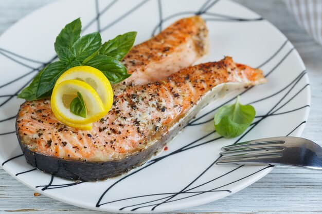 Grilled Salmon steak with lemon and herbs on white dish. Healthy food concept.