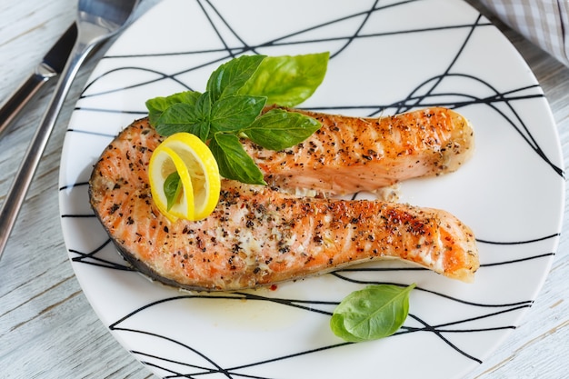 Grilled Salmon steak with lemon and herbs on white dish. Healthy food concept.