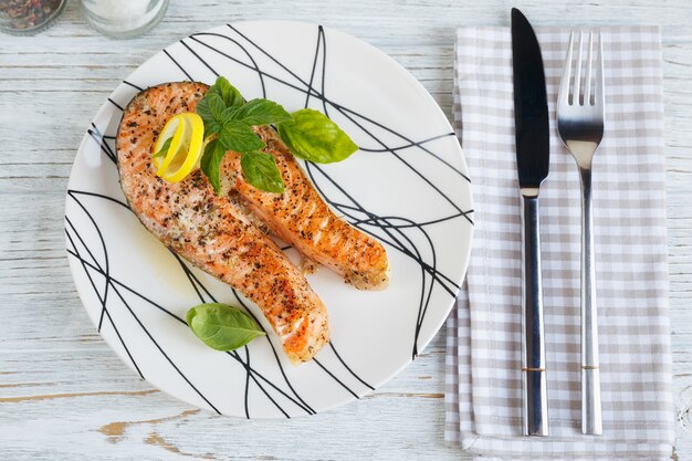 Foto bistecca di color salmone alla griglia con limone ed erbe aromatiche sul piatto bianco. concetto di cibo sano.