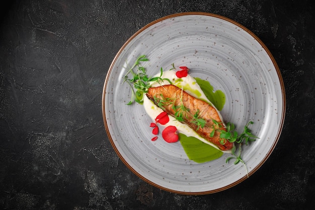 Grilled salmon steak with spices and a sprig of peas on a dark stone table