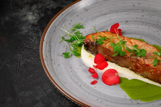 Grilled salmon steak with spices and a sprig of peas on a dark stone table