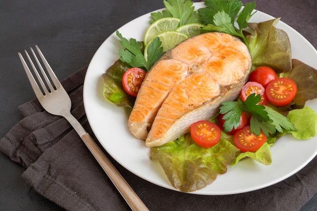 Grilled salmon steak with vegetables. on a dark table.