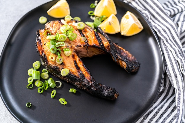 Grilled salmon steaks garnished with green onions on a black plate.