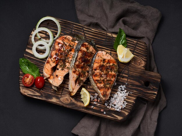 Grilled salmon with lemon salt tomatoes onion and herbs on cutting board on grey background