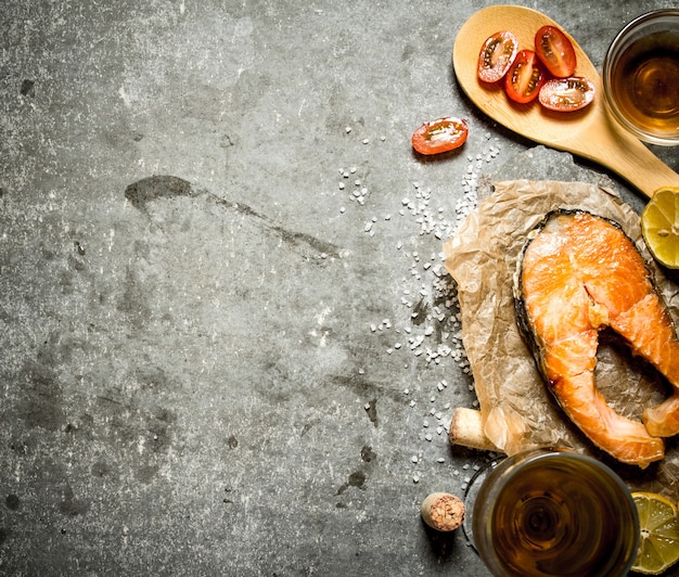 Grilled salmon with olive oil, tomatoes, lemonnd spices on stone table.