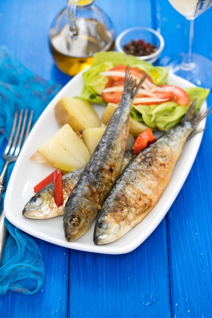 Grilled sardines with boiled potato and salad on white plate