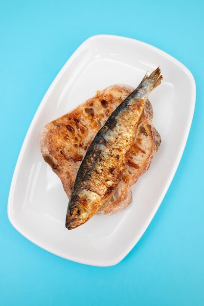 Grilled sardines with sauce on fresh bread on white dish