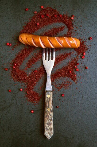 Grilled sausage on fork in spices on black background.