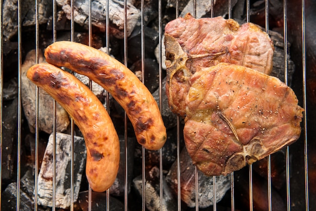 Photo grilled sausage and pork chop on the flaming grill