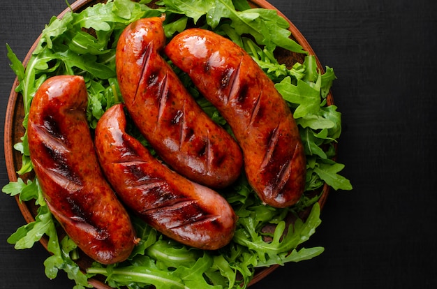 Grilled sausages and arugula on black background. Top view.