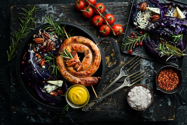 Grilled sausages and baked red cabbage with cheese rosemary and cranberries on a black plate Traditional German dish Top view On a black stone background