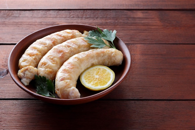 Grilled sausages on clay plate Fried chicken sausages with lemon and parsley on wooden background Copy space
