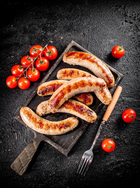 Grilled sausages on a cutting board with tomatoes