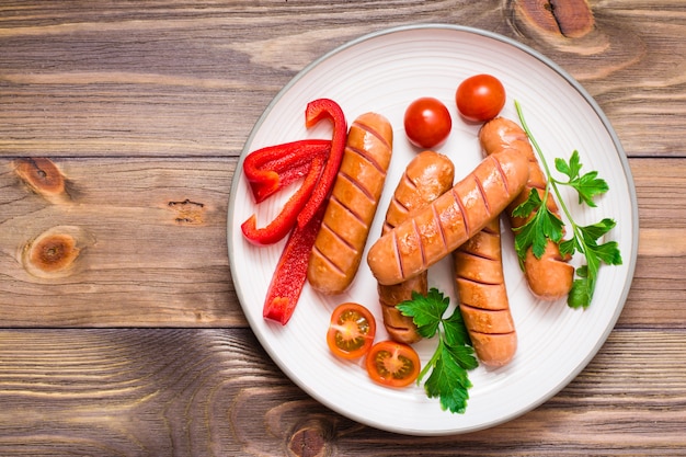 Grilled sausages, fresh tomatoes, peppers and parsley on a plate on a wooden table. Top view.