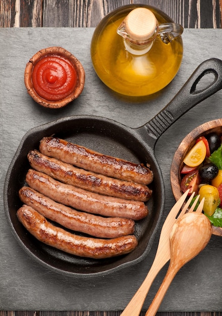 Grilled sausages in a pan and vegetable salad top view