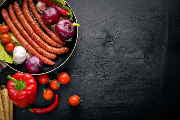 Grilled sausages in a pan with fresh vegetables Wooden on the black surface Top view