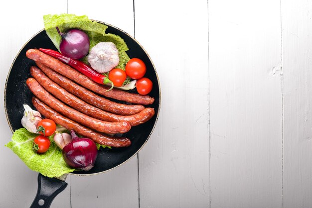 Grilled sausages in a pan with fresh vegetables Wooden on the black surface Top view