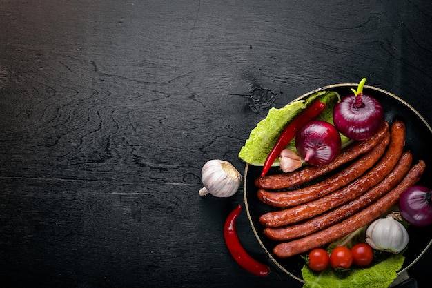 Жареные сосиски на сковороде со свежими овощами Деревянная поверхность Вид сверху