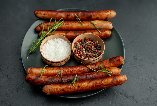 Grilled sausages on a plate with spices and rosemary on a stone table