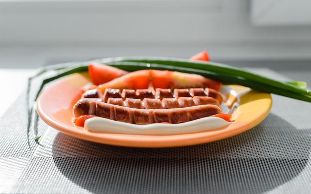 Grilled sausages tomatoes green onions with ketchup and mayonnaise on a plate inside Closeup selective focus