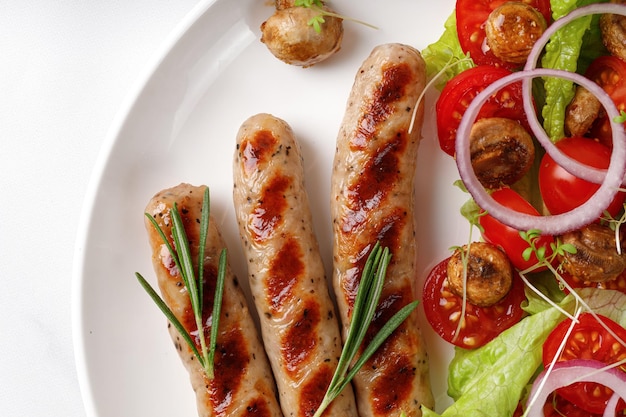 Grilled sausages and vegetable salad with lettuce and tomatoes on white plate close up Top view BBQ